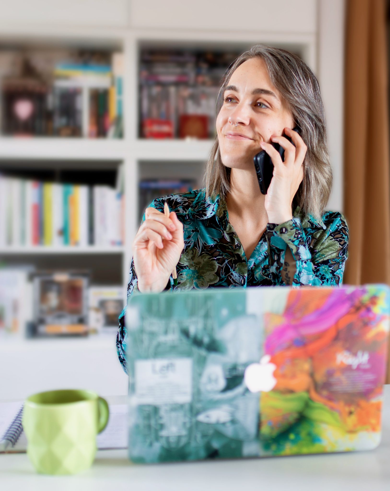 Persona sorridente al telefono, davanti al suo PC e tazza di caff&egrave;